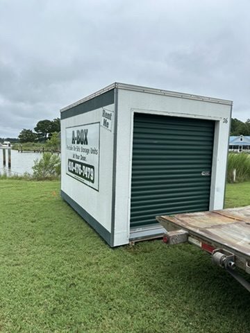 A Box delivery trailer placing a portable storage container on a waterfront property lawn in Maryland