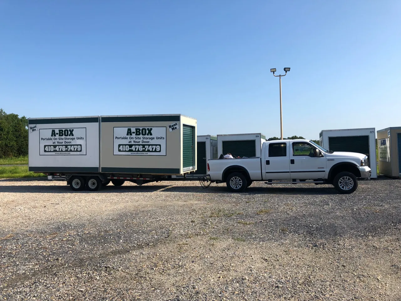 A Box pickup truck towing a trailer loaded with two branded portable storage containers out of the Cambridge, Maryland yard