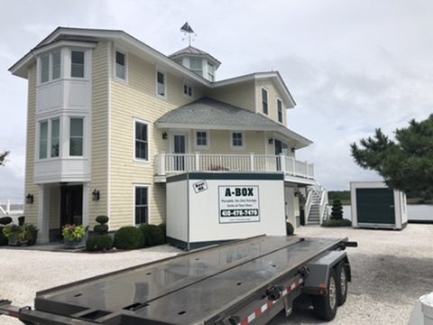 A Box tilt-bed trailer hauling a loaded portable storage container to a coastal beach house